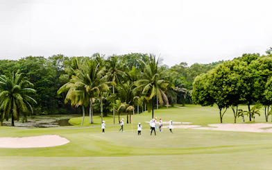 Golfers on the green at Batam Island Country Club, surrounded by palm trees.