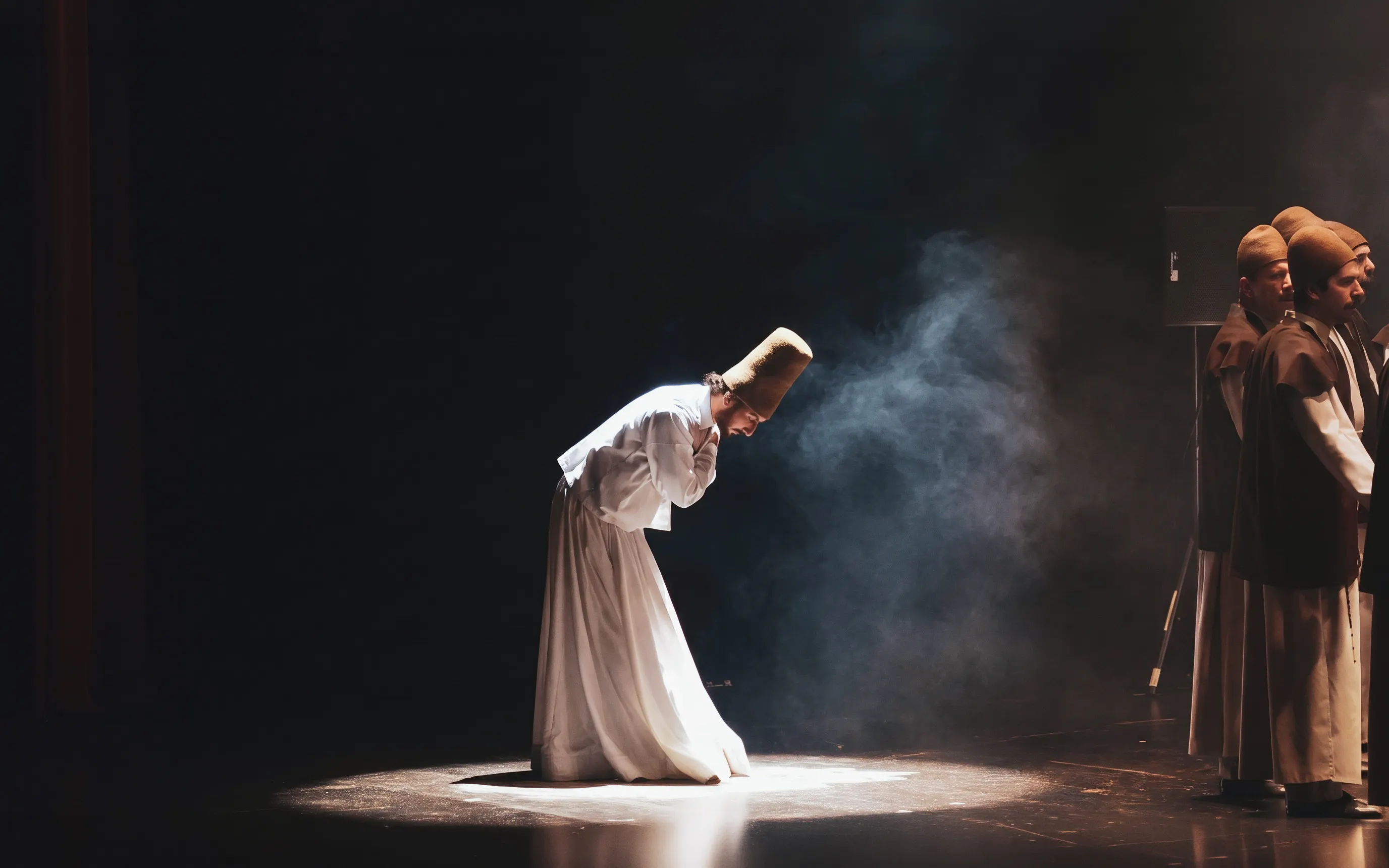 Dervish bowing during a traditional dance ceremony with others in the background.