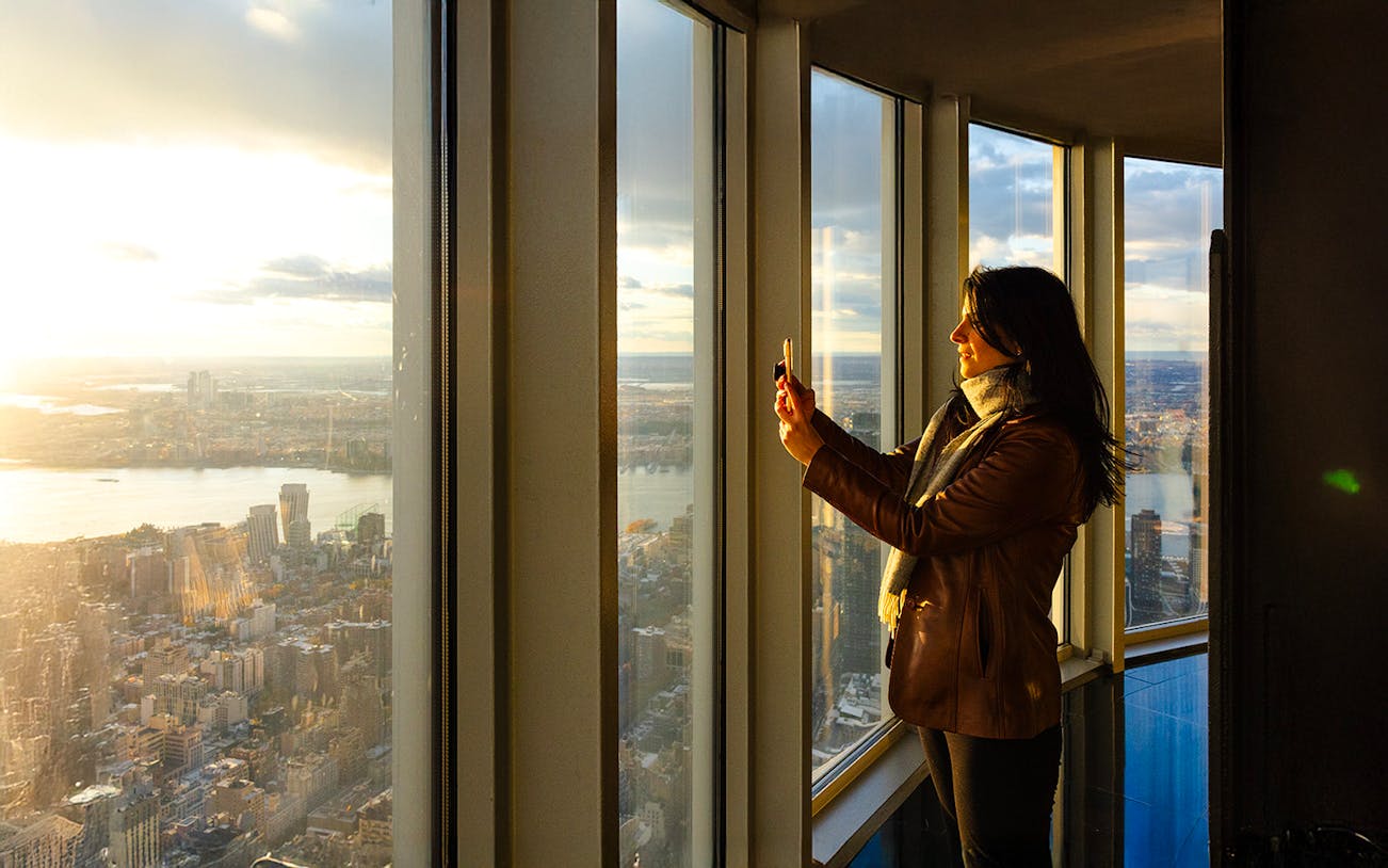 Guest taking photo at Empire State Building observatory with city view.