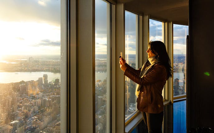 Guest taking photo at Empire State Building observatory with city view.