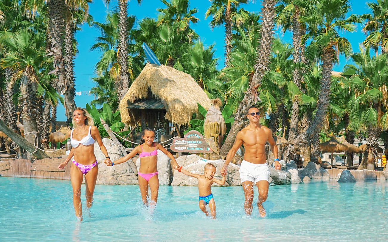 Family enjoying a day at Caribe Bay water park, running through a pool surrounded by palm trees.