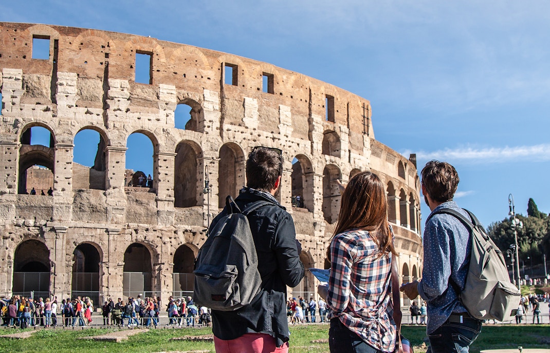 Three tourists with backpacks in front of the Colosseum, Rome.