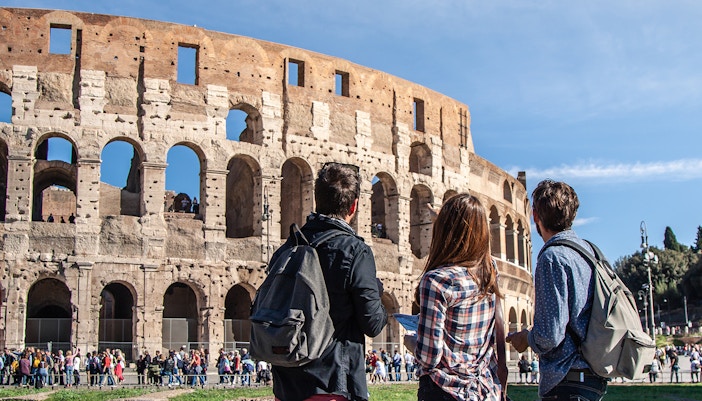 Three tourists with backpacks in front of the Colosseum, Rome.
