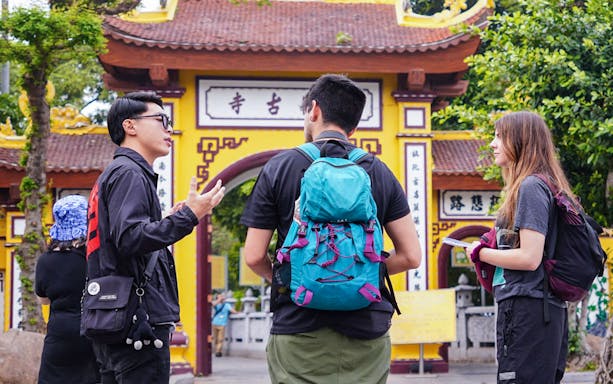 Tour guide with tourists at a historic temple entrance in Hanoi.