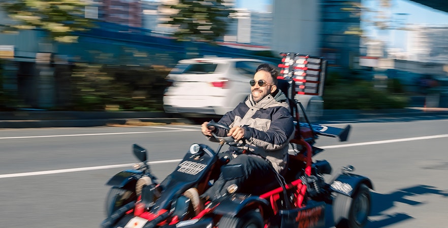 Man driving a gokart on Asakusa Tour, Tokyo street with cityscape in background.