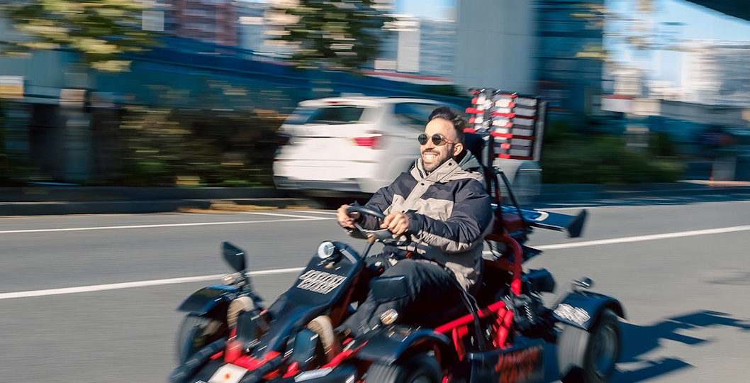 Man driving a gokart on Asakusa Tour, Tokyo street with cityscape in background.