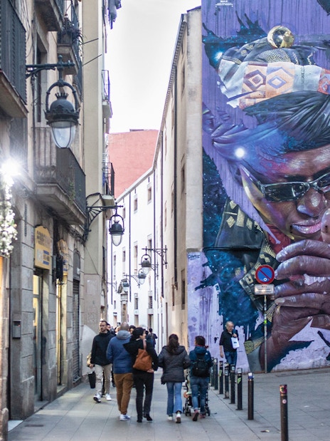 Street art mural in Raval, Barcelona, with people walking along a narrow alley.