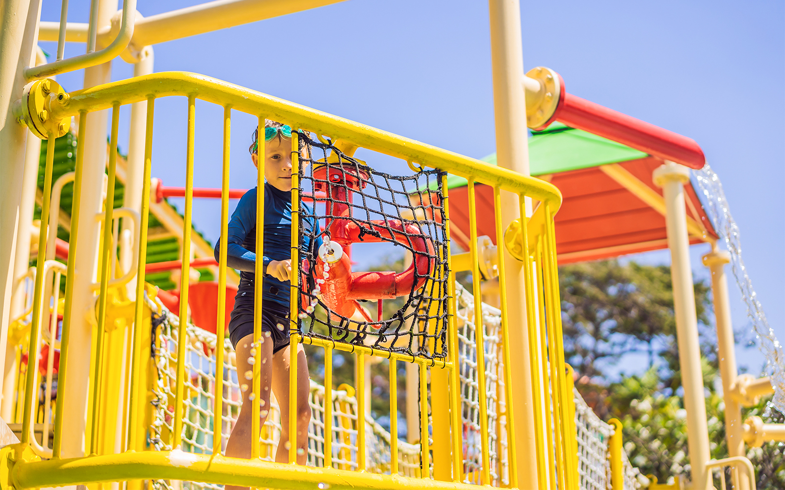 Child playing on a colorful water park structure with netting and slides.