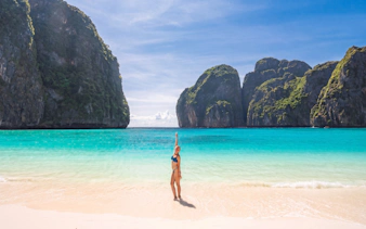 Person on a sandy beach with turquoise water and limestone cliffs, Phi Phi Islands, Phuket.