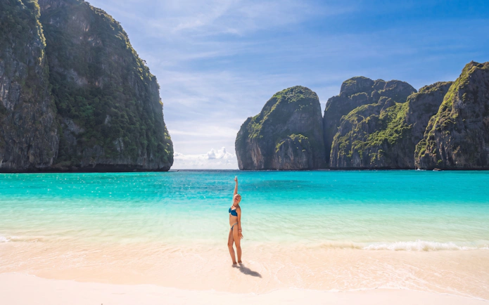 Person on a sandy beach with turquoise water and limestone cliffs, Phi Phi Islands, Phuket.