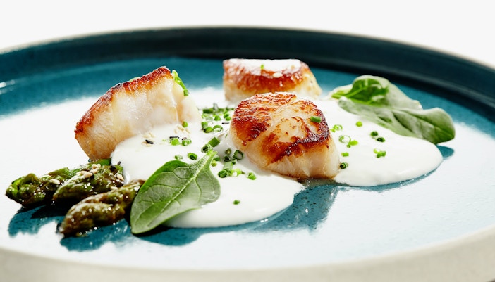 Grilled scallops with asparagus and creamy sauce on a blue plate.