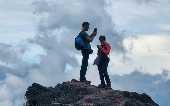 Trekking couple on a rocky peak in Mu Cang Chai, capturing views of terraced rice fields.