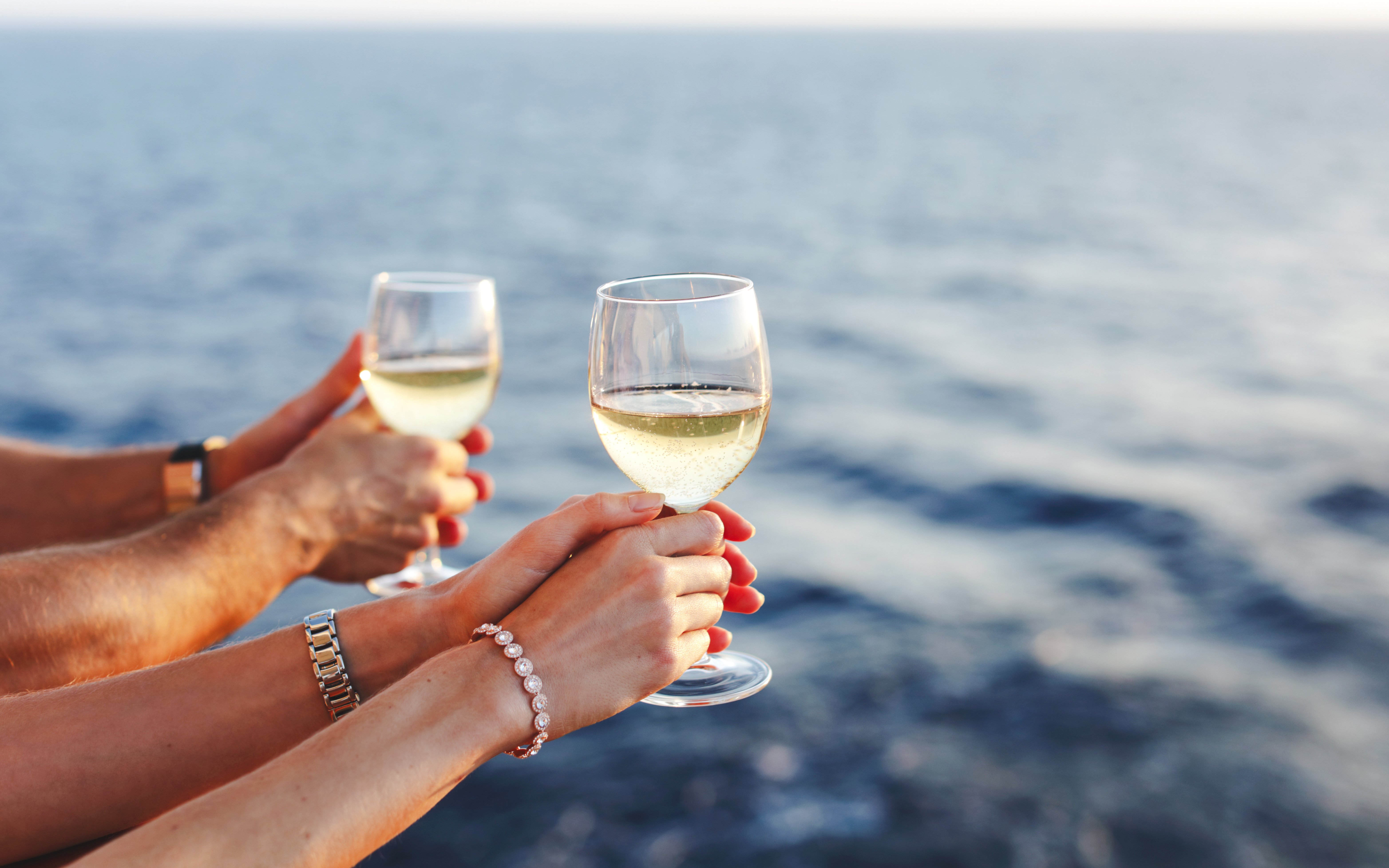 Hands holding wine glasses on a cruise ship with ocean view.