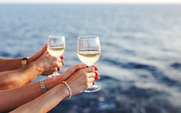 Hands holding wine glasses on a cruise ship with ocean view.