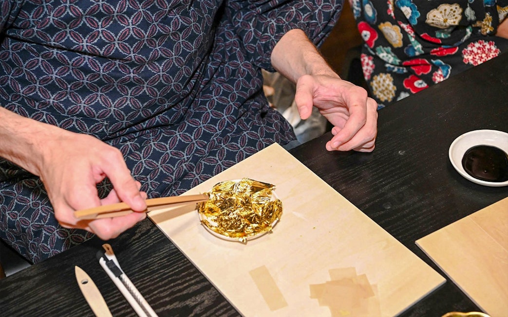 Hands using chopsticks to apply gold leaf on a small plate.