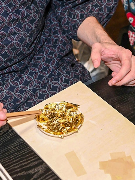 Hands using chopsticks to apply gold leaf on a small plate.
