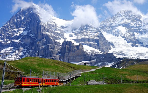 Red train on Jungfrau Railway with snow-capped mountains in Jungfraujoch, Switzerland.