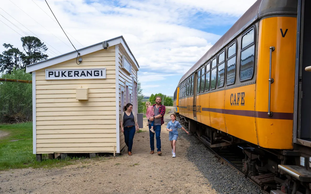 Family walking by Pukerangi station next to Taieri Gorge train, New Zealand.