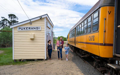 Family walking by Pukerangi station next to Taieri Gorge train, New Zealand.