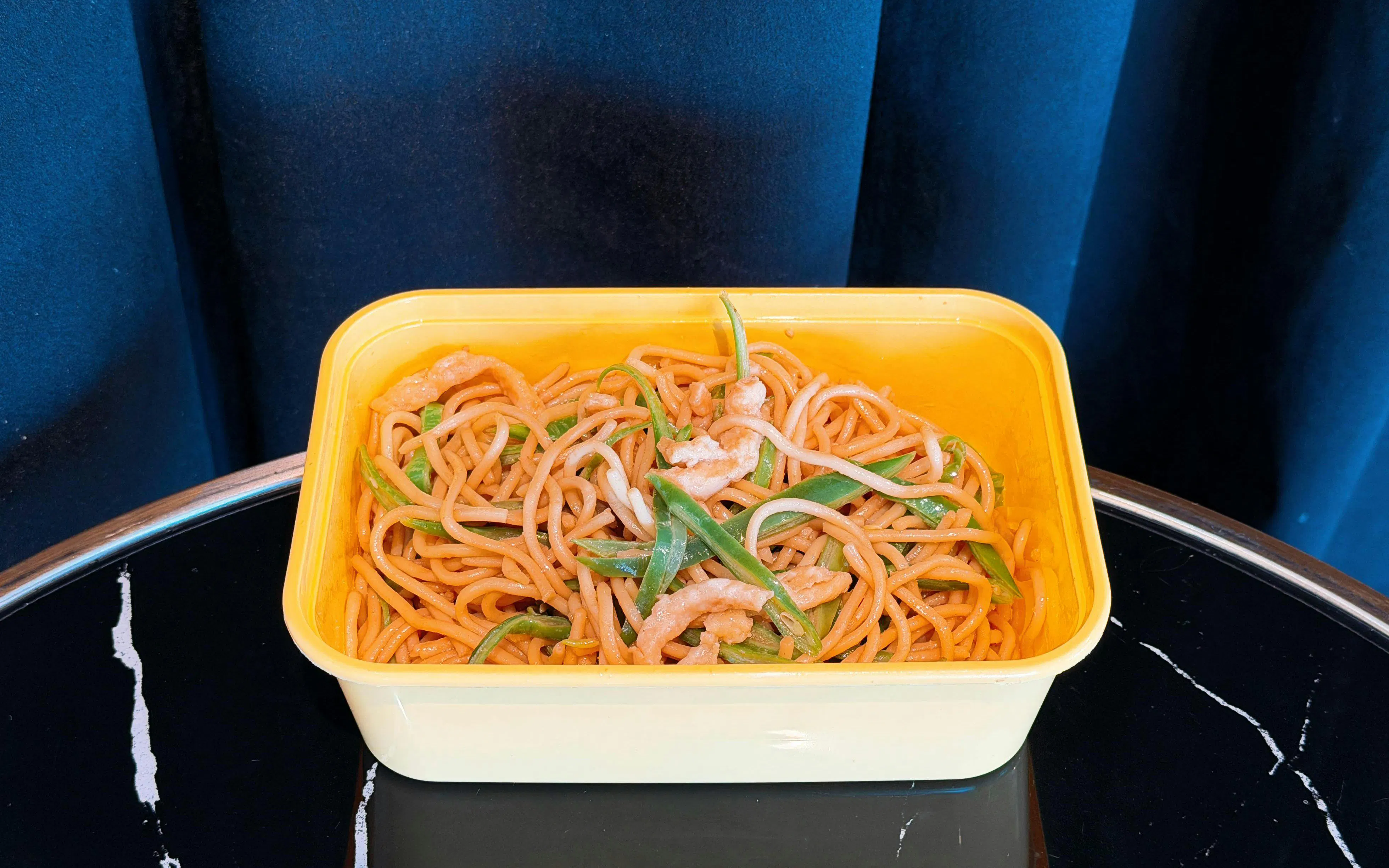 Noodles with vegetables and shrimp in a yellow container at Barcelo Lounge Beijing Airport.
