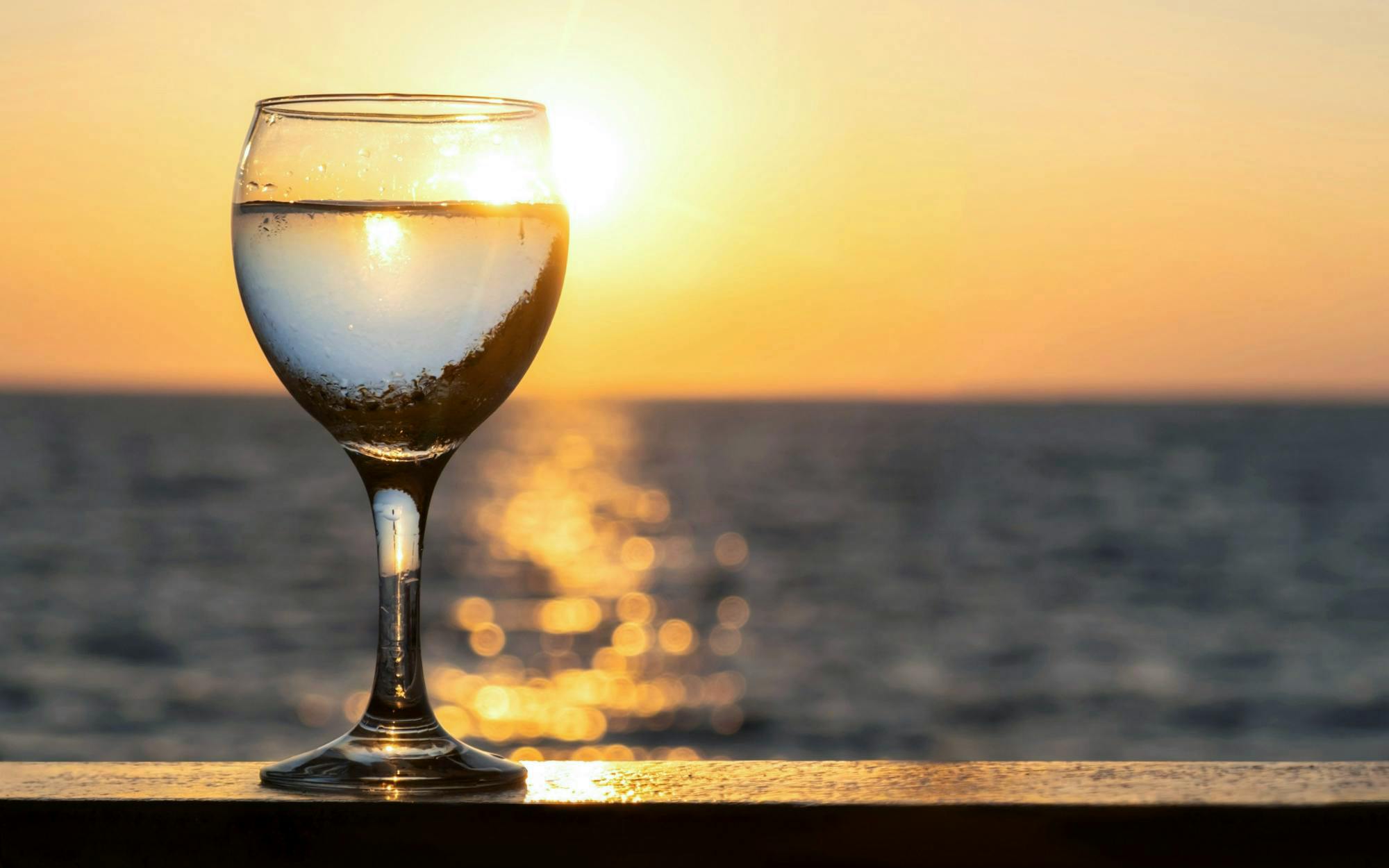 Wine glass on railing with sunset over Blue Lagoon, Ayia Napa cruise.