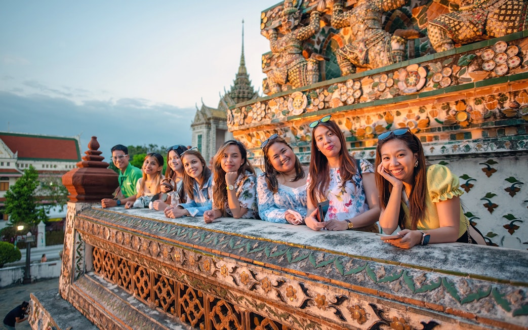 Group enjoying sunset at Wat Arun, Bangkok, with intricate temple details in view.