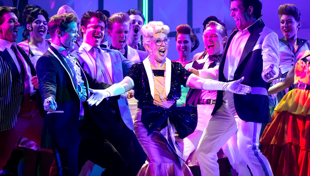 Cast performing a lively scene from the musical "Grease" on stage.