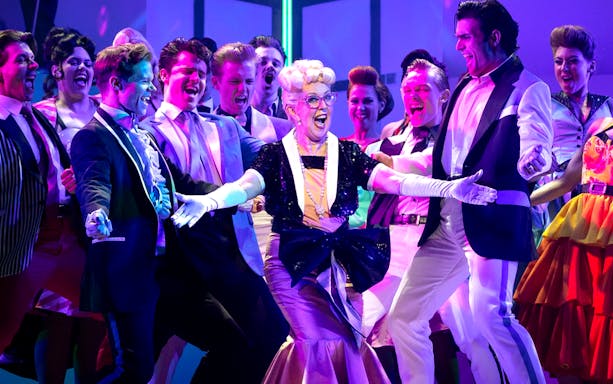 Cast performing a lively scene from the musical "Grease" on stage.