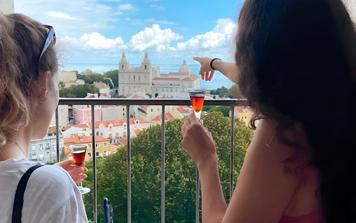 Women enjoying drinks with a view of São Jorge Castle Church in Lisbon.