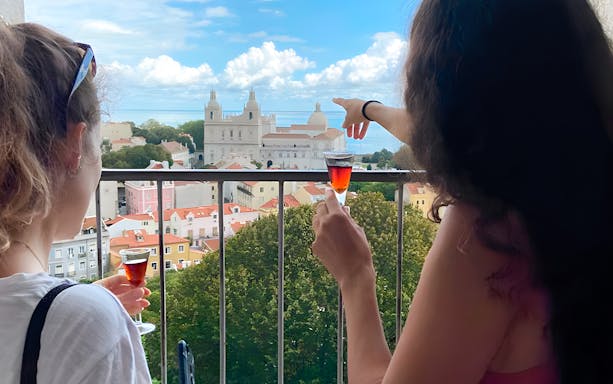 Women enjoying drinks with a view of São Jorge Castle Church in Lisbon.