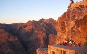 Mount Sinai sunrise view with tourists resting on a rocky ledge during a guided ascent.