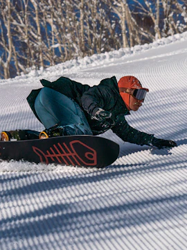 Snowboarder carving down a groomed slope in Hokkaido, Japan.