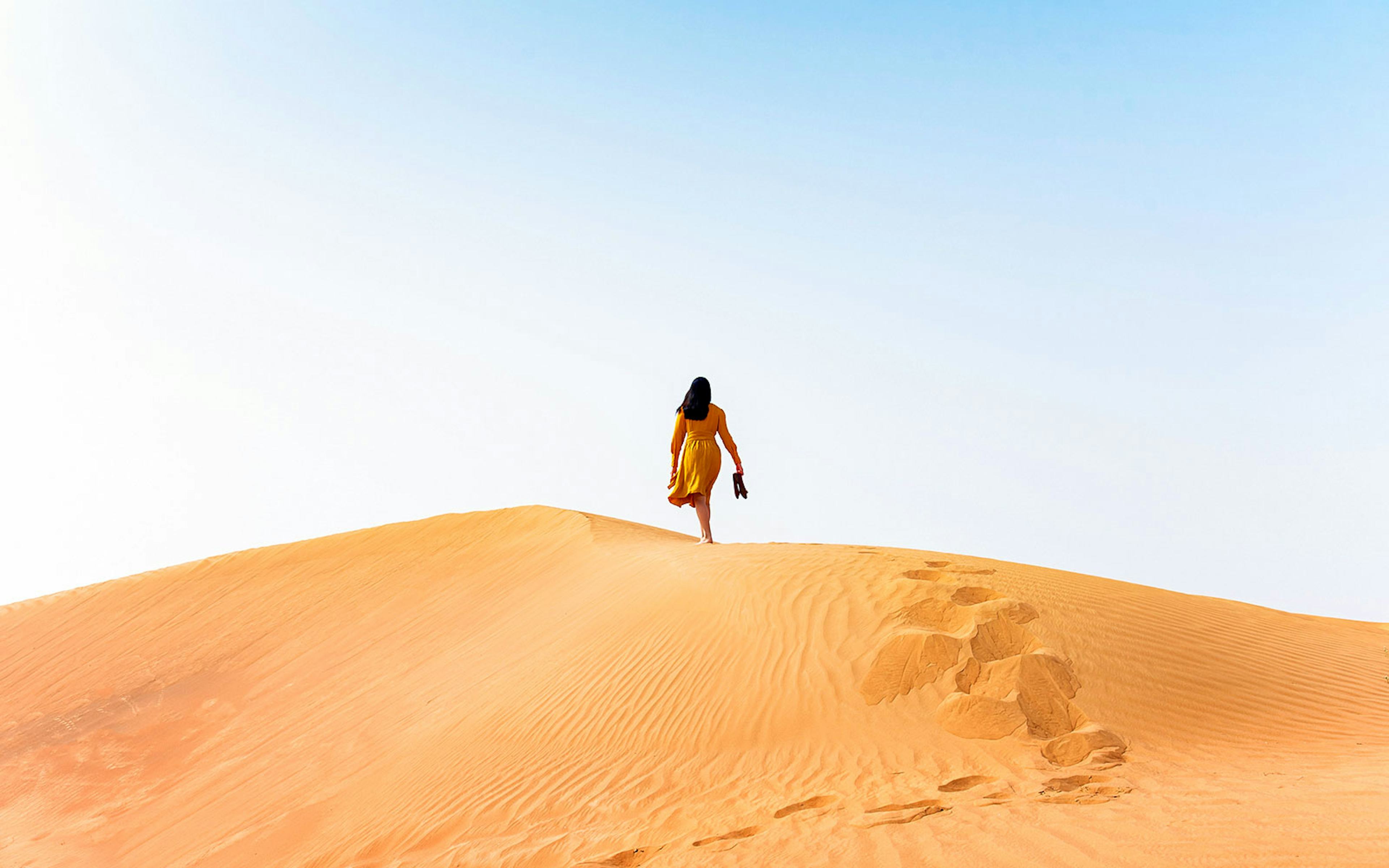 Woman walking on sand dune in desert.