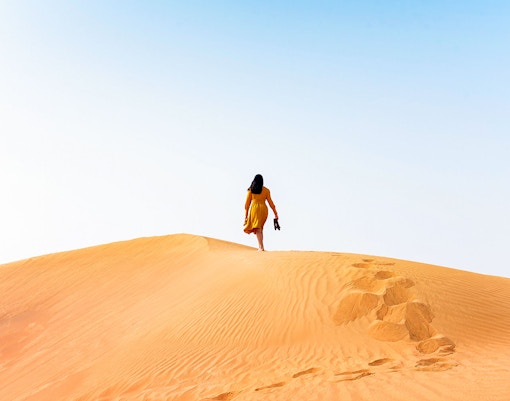 Woman walking on sand dune in desert.