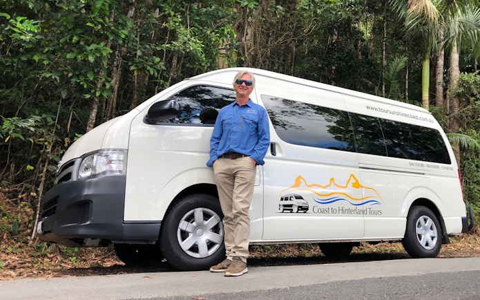 Tour guide standing beside a Coast to Hinterland Tours van for Eumundi Markets transfer.