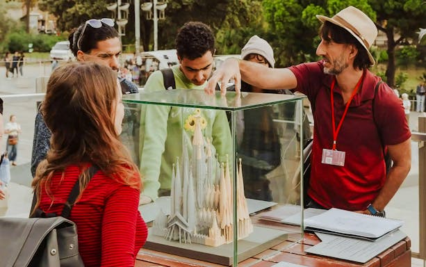 Tour guide explaining Sagrada Familia model to visitors in Barcelona.