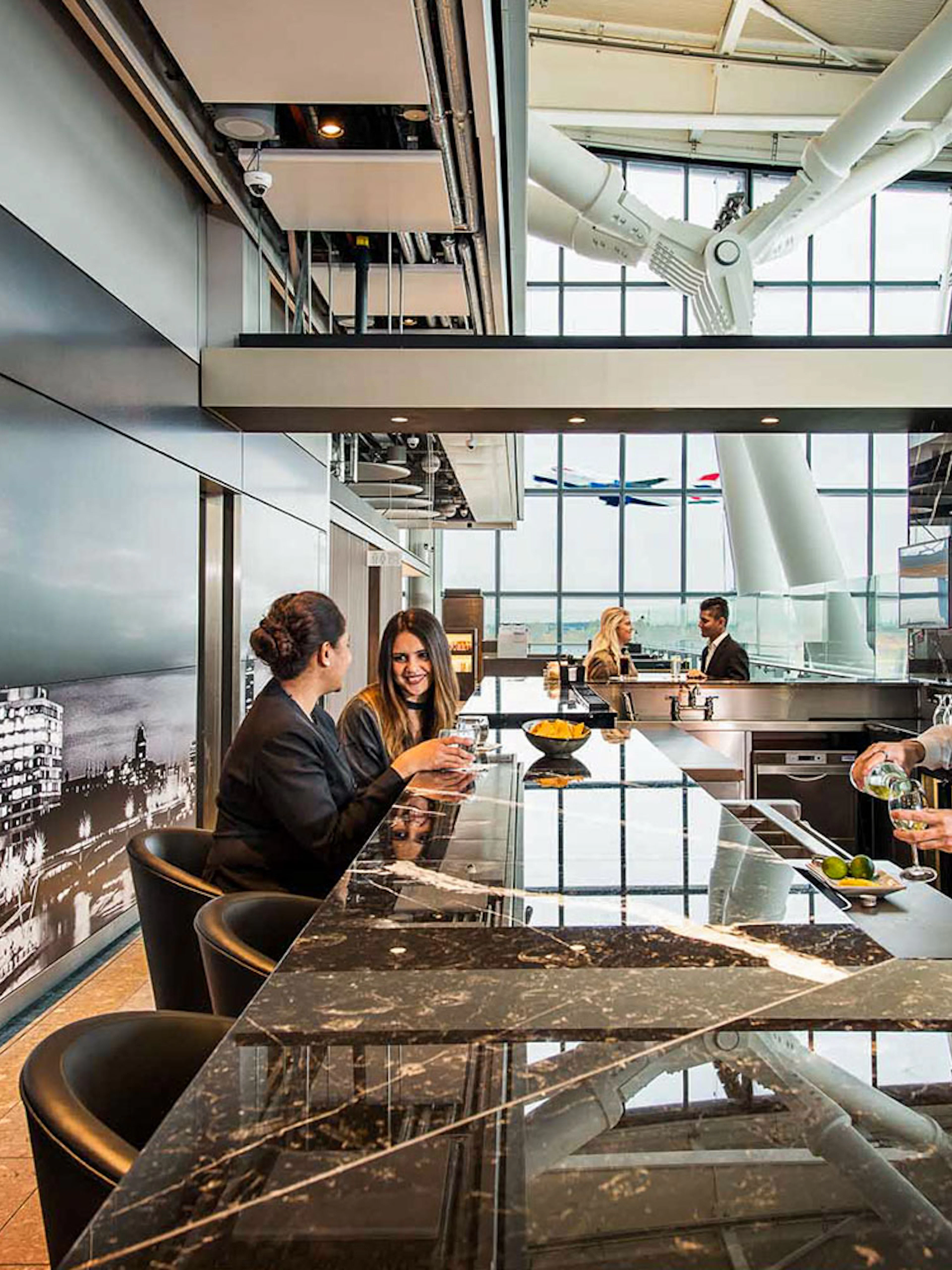 Heathrow Plaza Premium Lounge bar with bartender serving drinks and guests seated at the counter.