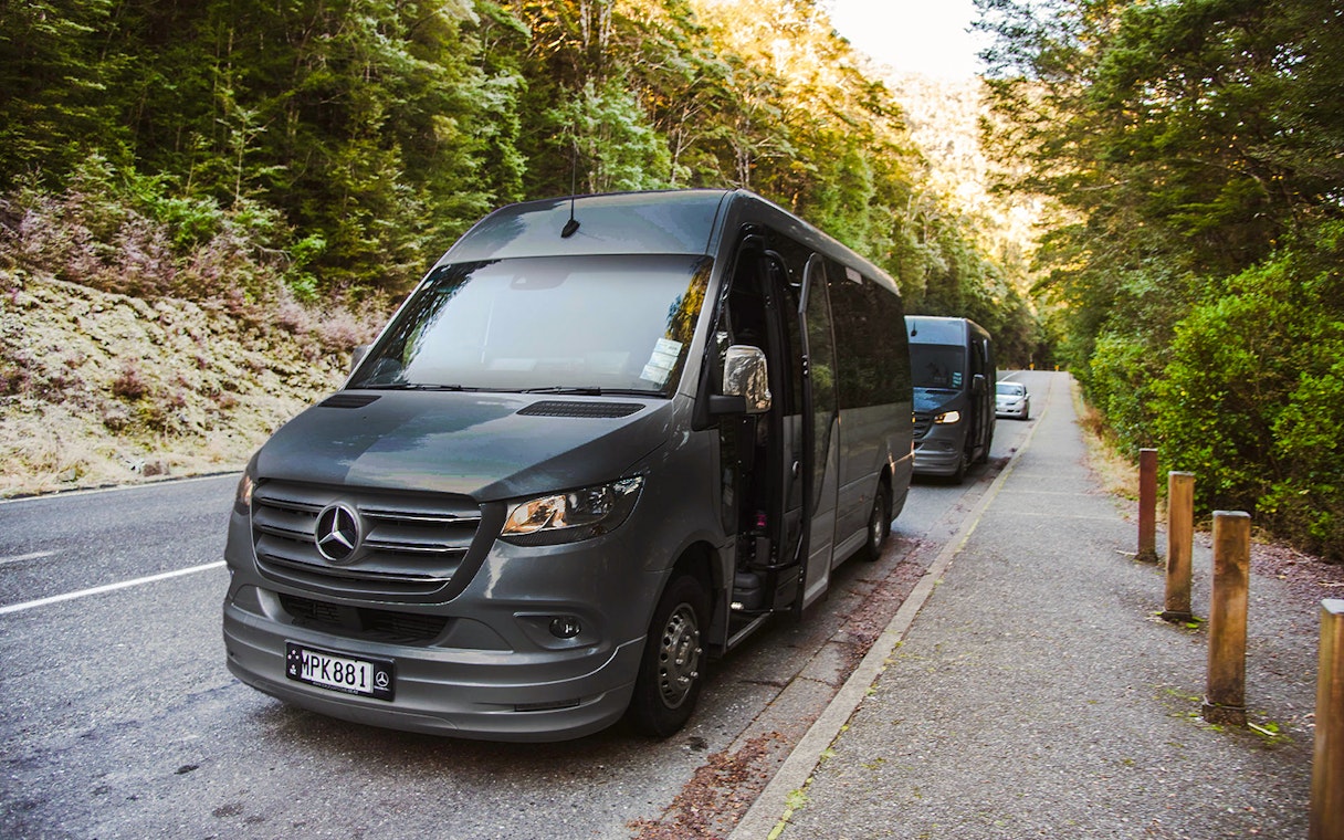 Luxury coach with glass roof parked on scenic road, Milford Sound.