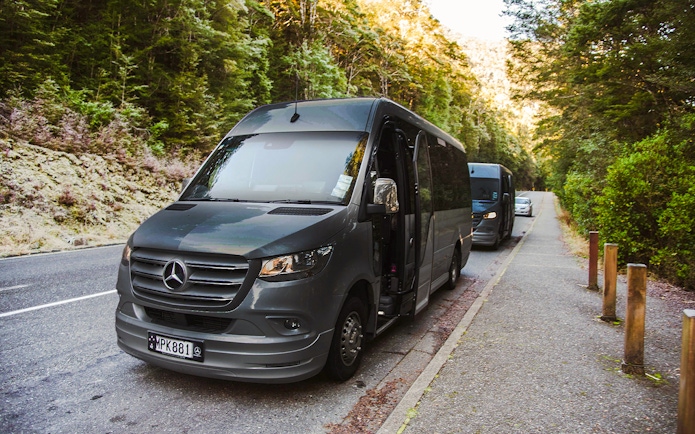 Luxury coach with glass roof parked on scenic road, Milford Sound.