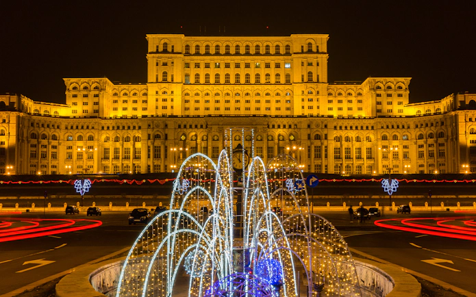 Palace of Parliament in Bucharest illuminated at night with festive lights in the foreground.