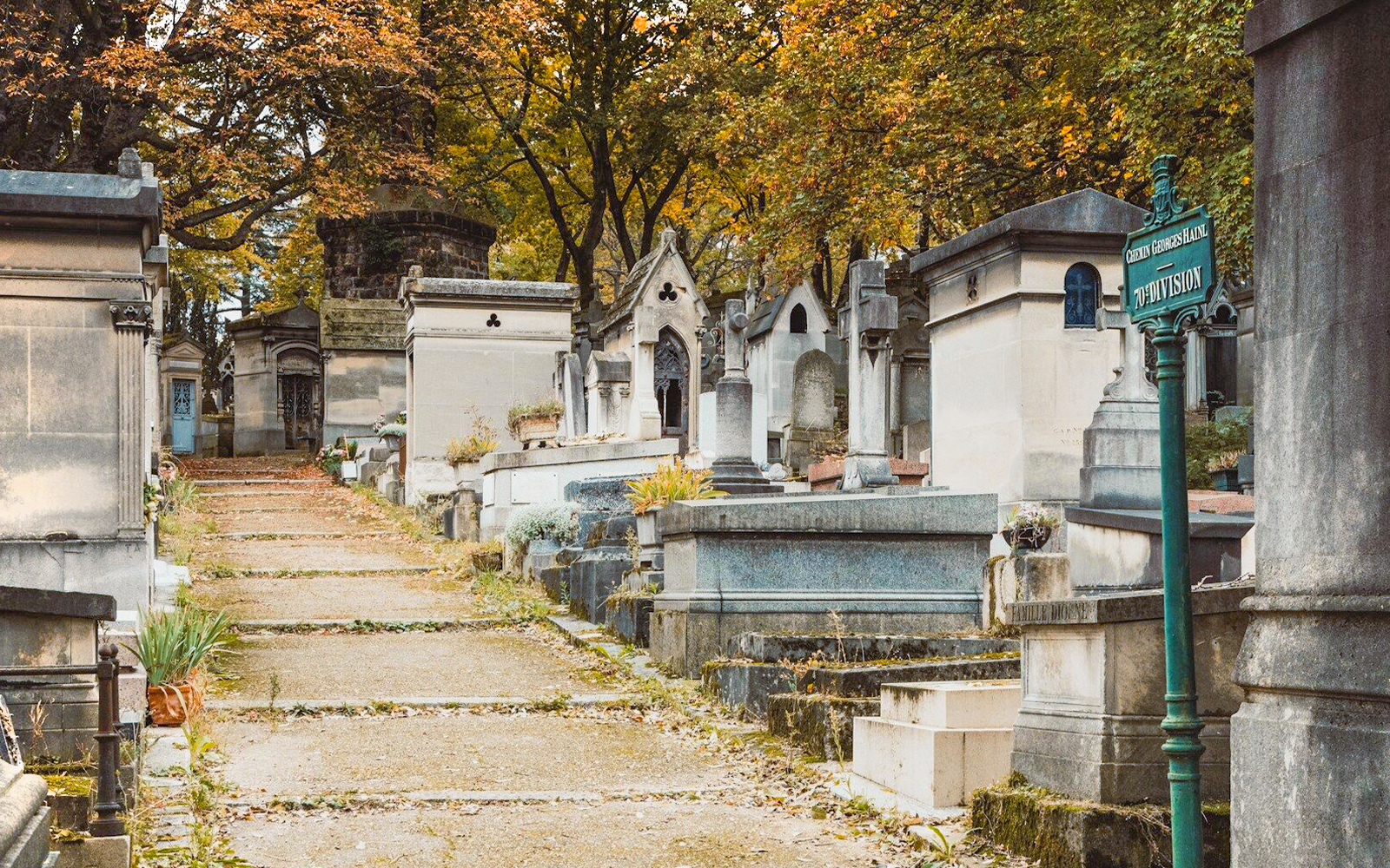 Pathway through tombs at Père Lachaise Cemetery, Paris, with autumn trees overhead.