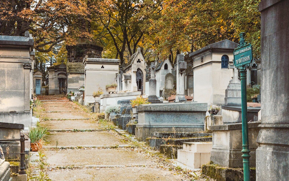 Pathway through tombs at Père Lachaise Cemetery, Paris, with autumn trees overhead.