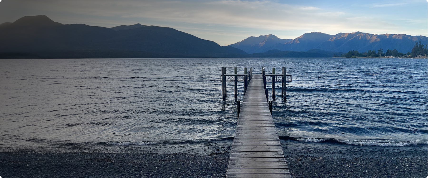 Wooden pier extending into Lake Te Anau with mountains in the background.