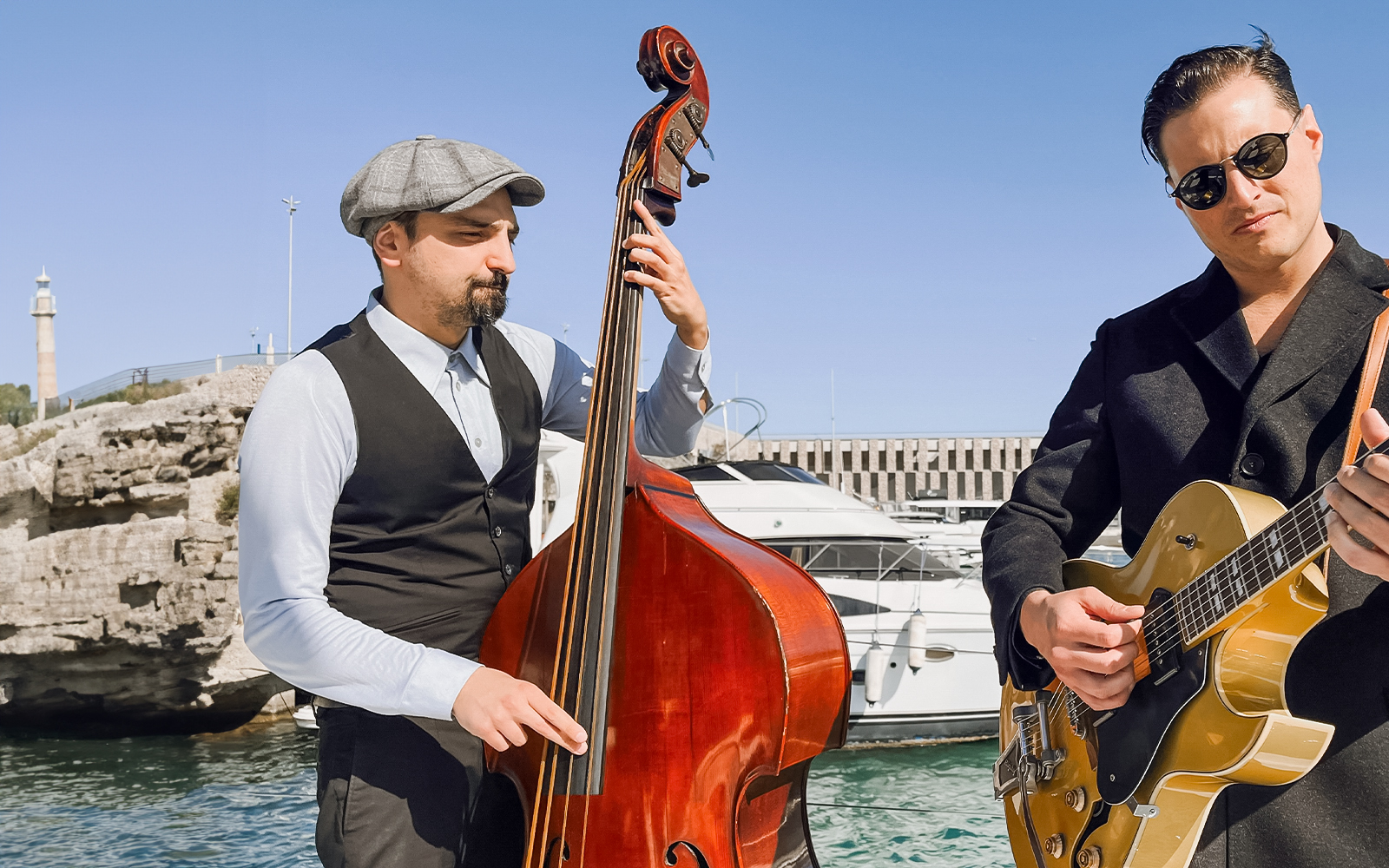 Musicians playing double bass and guitar on a catamaran in Barcelona harbor.