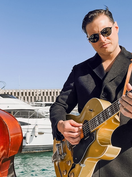 Musicians playing double bass and guitar on a catamaran in Barcelona harbor.