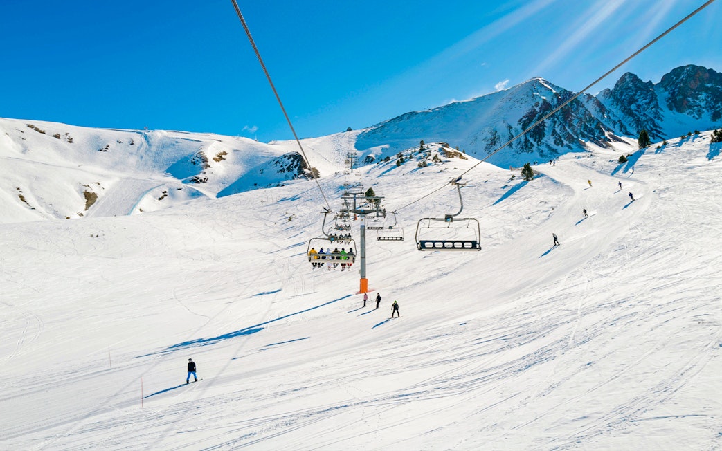 Skiers on a lift with snowy mountains in Andorra.