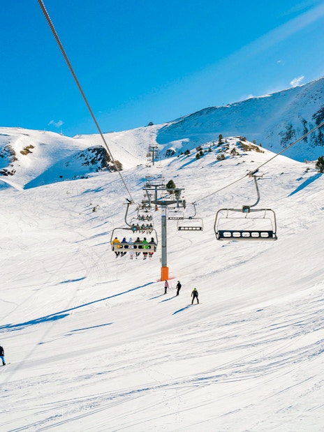 Skiers on a lift with snowy mountains in Andorra.
