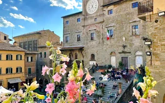 Piazza della Repubblica in Cortona with flowers and people on steps, Tuscany.