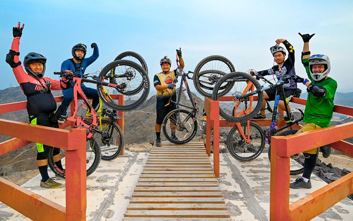 Group of cyclists holding mountain bikes at Fujairah Adventure Park viewpoint.
