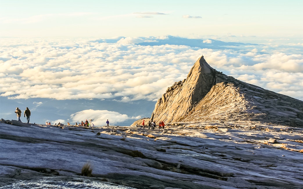 Hikers approaching the summit of Mount Kinabalu, surrounded by clouds.